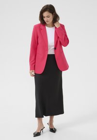 Světle růžový blazer s výstřihem do V, černá sukně a černé podpatkové mules. Hladká tkanina, přiléhavý střih a zapínání na jedno tlačítko.