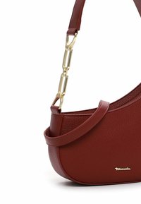 Borsa a spalla in ecopelle rossa con texture, dalla forma curvata, dettagli in catena dorata e una tracolla sottile e regolabile. Caratterizzata da un logo impresso.