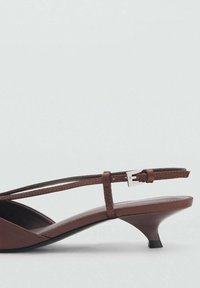 Hnědá slingback obuv s nízkým rozšířeným podpatkem. Obsahuje štíhlý pásek se stříbrnou sponou a špičatým designem špičky. Hladký kožený povrch.