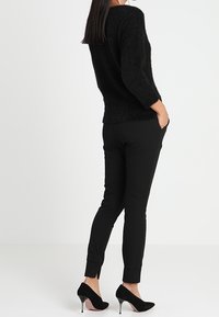 Un pull noir en laine moelleuse à manches trois-quarts associé à un pantalon noir fuselé et des escarpins à bout pointu. Textures lisses avec une coupe ajustée.