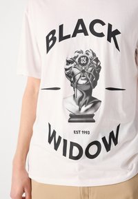 Hvit bomulls T-skjorte med et grafisk bilde av en klassisk byste med et edderkoppoverlegg, og fet tekst "BLACK WIDOW" over og "EST 1993" under.