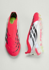 Φωτεινά κόκκινα και λευκά ποδοσφαιρικά παπούτσια με μαύρες λεπτομέρειες, υφασμένο επάνω μέρος και διάφανα τάπες στη σόλα, εμφανιζόμενα από πάνω και από την πλευρά.