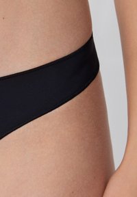 Czarny dół bikini wykonany z gładkiego materiału, charakteryzujący się niskim stanem, bezszwowym pasem i dyskretnym wykończeniem.
