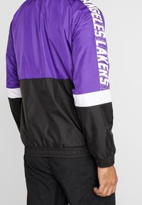 Lila och svart vindjacka med en vit rand; "Los Angeles Lakers" logotyp längs vänster ärm. Elastiska manschetter och nederkant.