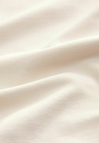 Šviesiai smėlinė medžiaga, lygaus paviršiaus, smulkus briaunų raštas, drapiruota švelniais raukšlėmis, demonstruojanti švelnią, vienodą spalvą ir matinį paviršių.