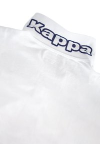 Fehér pólóing texturált anyagból, kék "Kappa" logóval a gallérján. A gallér merev, álló kivitelű.