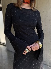 Robe noire avec de longues manches évasées, ornée de points argentés. Elle possède un col rond et est accessorisée de bracelets métalliques.