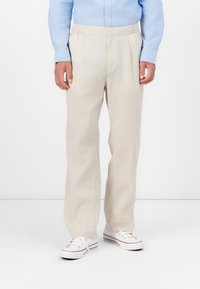 Pantalones de lino beige con una cinturilla elástica, con un corte relajado y bolsillos laterales, combinados con zapatillas blancas.