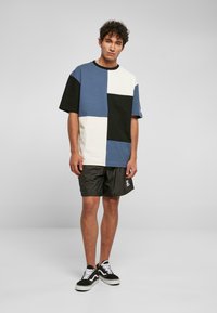 Mėlynos, juodos ir baltos spalvų blokais išskirta trumpa rankovė t-shirt; derinama su juodais šortais ir juodais sportbačiais su baltais raišteliais. Kasdieniška, laisva fit.