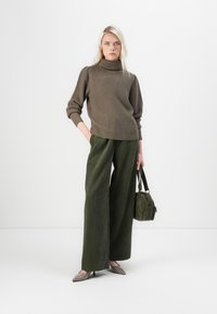 Olivgrön vida kordbyxor som matchas med en brun ribbad polotröja. Modellen håller en liten mörkgrön väska. Spetsiga beige ballerinaskor.