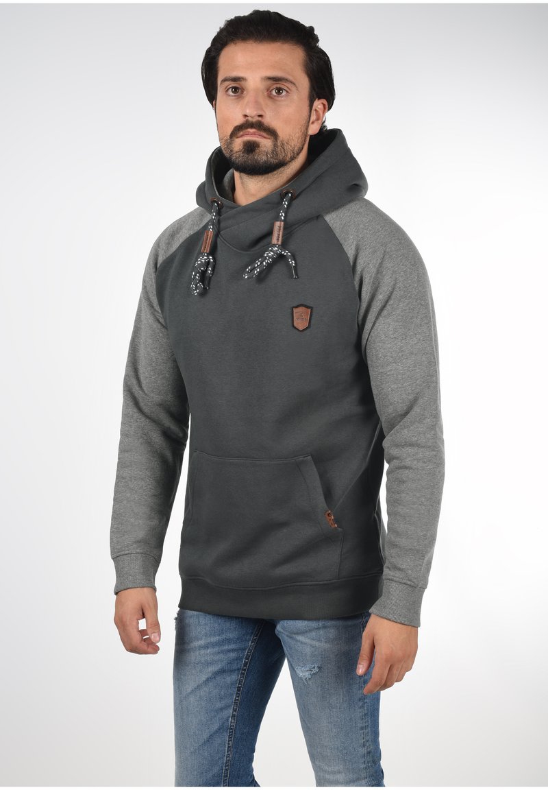 Sudadera gris oscuro con mangas gris claro, con un bolsillo tipo canguro en el frente, capucha con cuerda ajustable y un emblema de cuero.