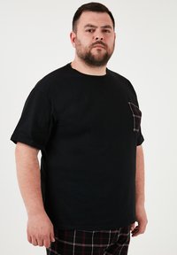 Czarna koszulka z krótkim rękawem, wykonana z gładkiej bawełny, z kieszenią w kratkę w kolorze czerwono-białym. Prosty dekolt w kształcie zaokrąglenia.