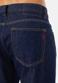 Mörkblå denimjeans med kontrasterande orange sömmar, med en bakficka med en röd logodetalj och en rak skärning.