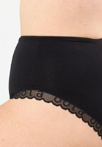 Svart bomullsunderkläder med spetsdetaljer, med en scalloped kant och halvgenomskinliga meshinslag längs midjebandet.