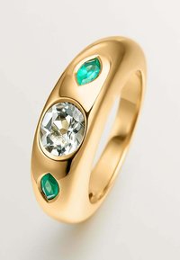 Anillo de oro que presenta una gran piedra preciosa redonda y clara en el centro, flanqueada por dos piedras verdes cortadas en forma de marquesa a cada lado. Acabado pulido y suave.