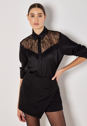 Black shirt with lace paneling and button closure, featuring a collar and long sleeves. Paired with black shorts and tights.