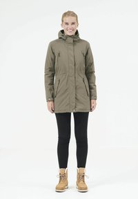 Olivgrön parka-jacka med dragkedja framtill, två sidofickor, huva och figursydd midja. Matchas med svarta leggings och bruna stövlar.