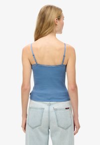 Blauwe geribbelde camisole met kantafwerking en verstelbare bandjes; gecombineerd met lichtblauwe high-waisted jeans met achterzakken en labeldetails.