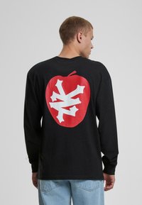 Schwarzes Langarm-T-Shirt mit einem großen roten Apfel-Graphic und einem weißen Schneeflocken-Design auf dem Rücken. Aus Baumwolle, lockere Passform.