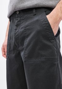 Fekete pamut nadrág egyenes szabással, elülső zsebekkel, finom varrásokkal és fém gombos derékpánttal.