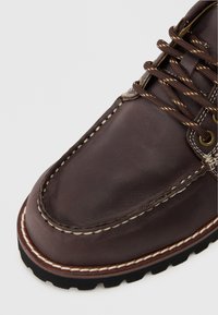 Braunes Leder-Schuh mit abgerundeter Zehenpartie, kontrastierenden Nähten, Metallösen und braunen Schnürsenkeln; Gummisohle mit strukturiertem Profil.