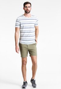 T-shirt rayé gris et blanc à manches courtes, associé à un short vert olive. Le modèle porte des baskets grises.