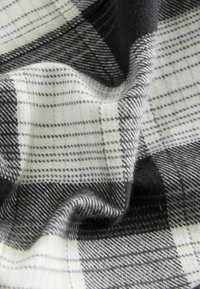 Tissu à carreaux noir et blanc avec une texture douce et duveteuse, montré en gros plan avec des plis et des froissements visibles.