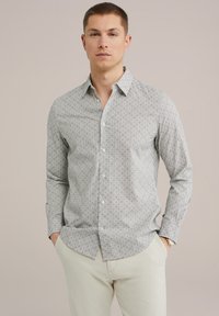 Camisa de botones en tela gris claro con un intrincado estampado geométrico. Mangas largas con puños de botón, bolsillo en el pecho y dobladillo recto.