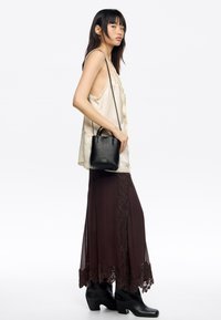 Czarna skórzana torebka o zdefiniowanym kształcie, z krótkimi uchwytami i długim paskiem, zestawiona z kremowym topem na ramiączkach i brązową spódnicą zdobioną koronką.