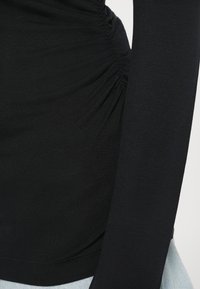 Top nero aderente a maniche lunghe con dettagli arricciati lungo il lato e una morbida texture, abbinato a un fondo in denim azzurro chiaro.