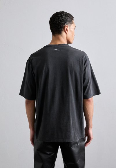 T-shirt en coton noir avec une coupe décontractée, des manches courtes et un col rond. Présente des accents blancs minimalistes au dos.