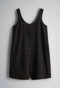Combinaison courte sans manches de couleur sombre avec un motif abstrait noir rappelant un zèbre, larges bretelles et encolure en V, suspendue contre un mur uni.