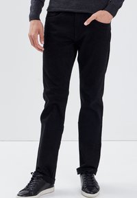 Schwarze Denim-Jeans mit schmalem Schnitt, ausgestattet mit einem klassischen Fünf-Taschen-Design und an den Knöcheln umgeschlagenen Säumen, kombiniert mit schwarzen Sneakers.