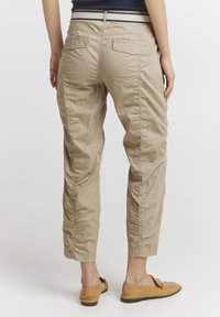 Pantalons kaki à coupe décontractée, dotés de poches arrière et d'une texture légèrement froissée. Associés à des chaussures beiges à enfiler pour un look décontracté.