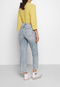 Pull en tricot jaune à manches trois-quarts associé à un jean taille haute bleu clair, avec des ourlets effilochés et des baskets montantes blanches.