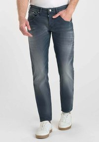 Jeans de mezclilla azul con un diseño de pierna recta, detalles desteñidos y estilo de cinco bolsillos. Llevados con zapatillas blancas para un look casual.