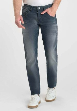 Jeans de mezclilla azul con un diseño de pierna recta, detalles desteñidos y estilo de cinco bolsillos. Llevados con zapatillas blancas para un look casual.