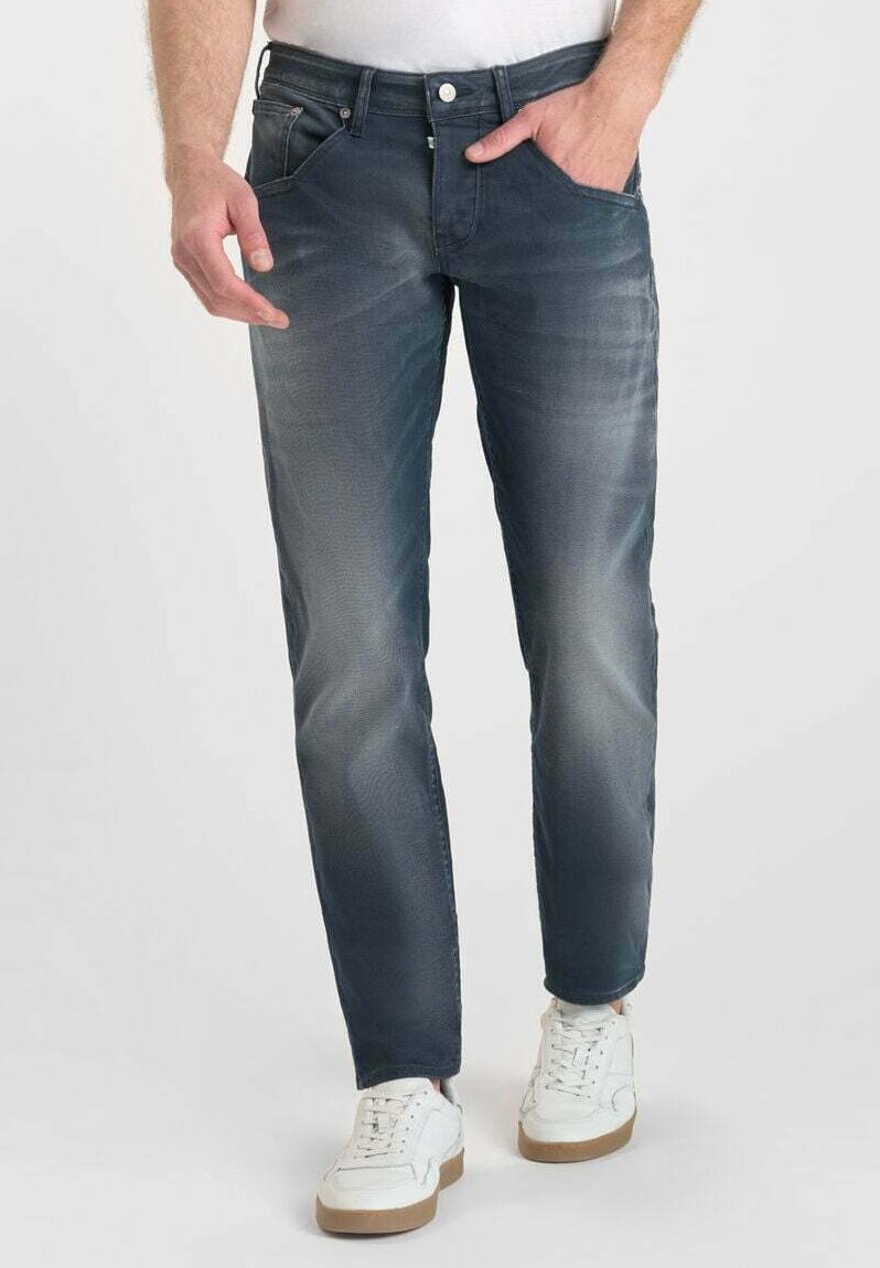Jeans de mezclilla azul con un diseño de pierna recta, detalles desteñidos y estilo de cinco bolsillos. Llevados con zapatillas blancas para un look casual.