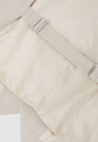 Beige stof med syede sømme og en justerbar rem med en rektangulær metalspænde.