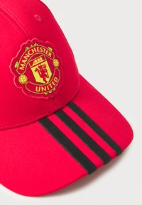 Boné de beisebol vermelho com o logotipo do Manchester United, três riscas pretas na pala e um acabamento texturizado. Fivela ajustável na parte de trás.