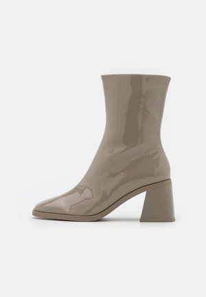 Beżowe lakierowane botki za kostkę z ostrym noskiem i grubym obcasem. Gładka tekstura i minimalistyczny design, odpowiednie do różnych stylizacji.