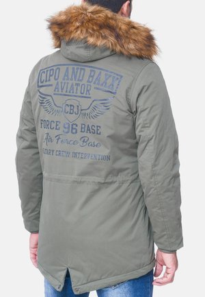 Groene bomberjack met een met bont afgewerkte capuchon. Kenmerken zijn gedrukte tekst en vleugelgraphics op de rug, met een gladde, licht gestructureerde afwerking.
