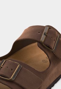 Καφέ σουέντ σανδάλι με δύο ρυθμιζόμενες μπρονζέ αγκράφες με την ετικέτα "Shepherd", με εργονομική σόλα και ανοιχτή μύτη.