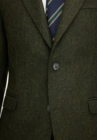 Grüner Fischgrät-Tweed-Blazer mit zwei Knöpfen, Reverskragen und Seitentaschen. Verfügt über eine strukturierte Oberfläche und dezente Farbvariationen.