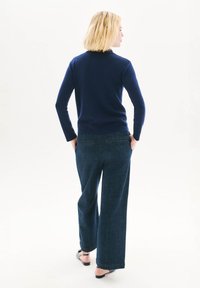 Donkerblauwe aansluitende trui met lange mouwen, gecombineerd met brede, donkerdenim broek met twee achterzakken en een eenvoudig ontwerp.