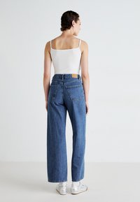 Light blue high-waisted wide-leg jeans with a denim texture, featuring a brown patch on the back waistband and two back pockets, worn with a white tank top.