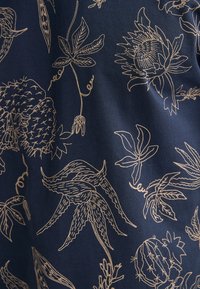 Marineblauwe stof met gouden botanische illustraties, met planten zoals cactussen, bloemen en bladeren. Soepele textuur met gedetailleerd lijnwerk.