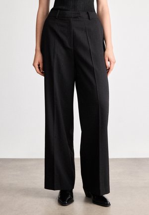 Mustad kõrge vöökohaga mustad ülikonnapasunaid, millel on voltimised ja lahtine istuvus. Valmistatud tekstureeritud materjalist, millel on peened täpid ja küljetaskud.