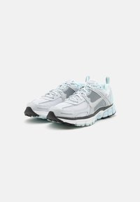 Light grey athletic shoes featuring a mesh upper, textured accents, and a black rubber sole with turquoise highlights for cushioning.
