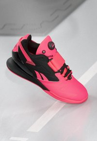 Ružovo-čierna atletická obuv s textúrovaným zvrškom, výrazným logom, elastickým systémom šnurovania a hrubou, zakrivenou podrážkou pre podporu.